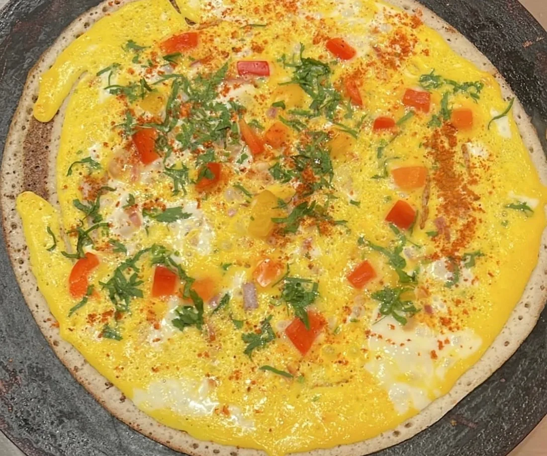 Egg dosa on the tawa, topped with tomato, onion, cilantro and chili
